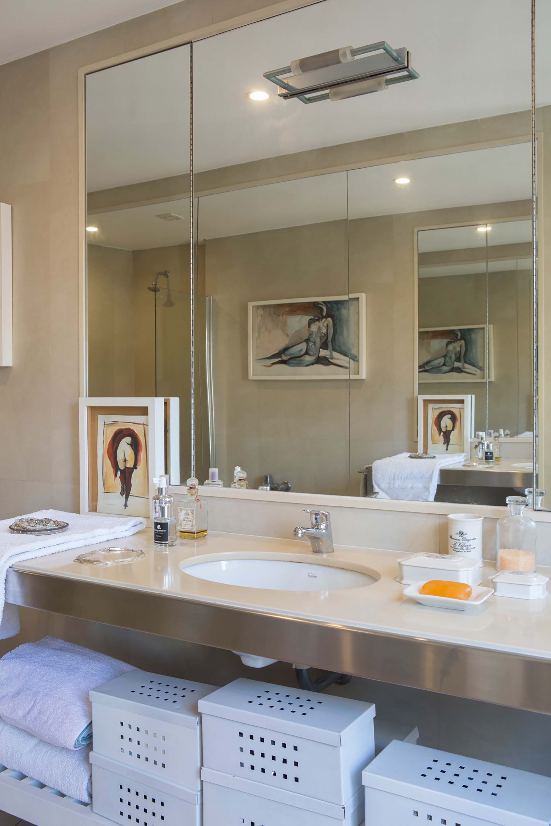 El arte también se cuela en el baño y se replica en el gran espejo pegado a filo que cubre la pared. Unas cajas decorativas permiten mantener todo en orden.