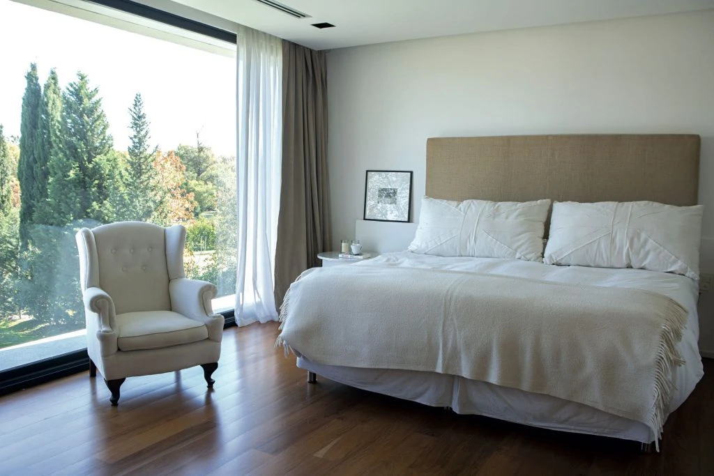 La suite tiene pisos de madera lustrados, cama con respaldo alto tapizado y mantas y almohadones blancos