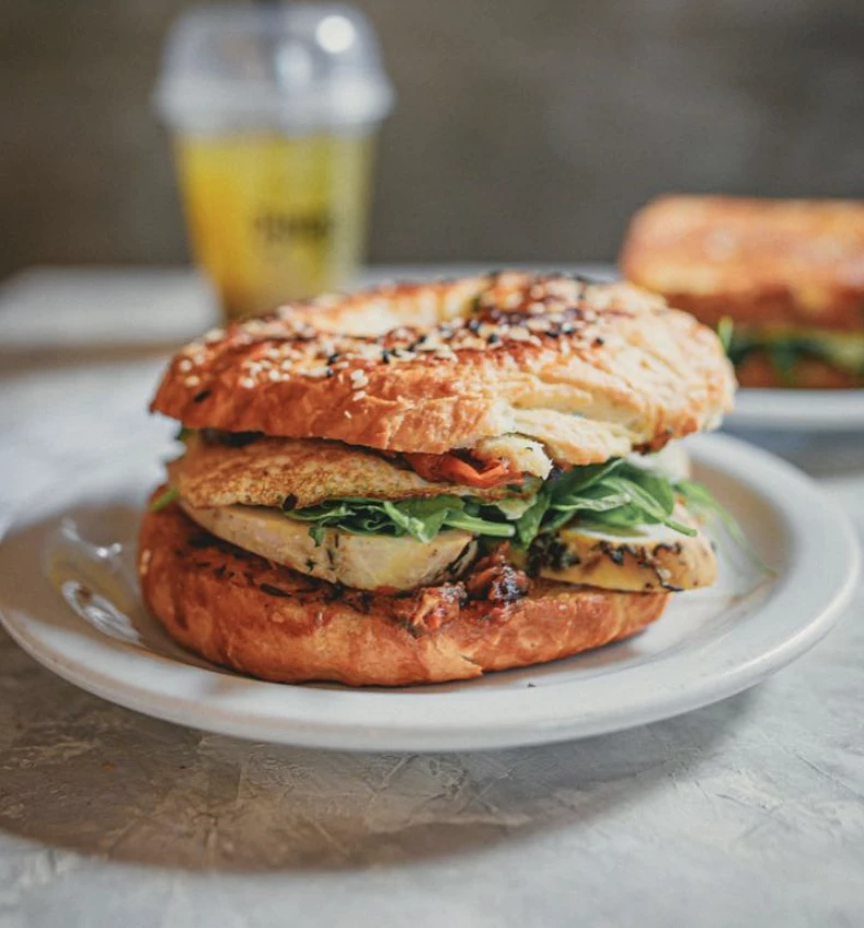 Bagel de pollo asado, palta, huevo, pesto de tomates secos y rúcula