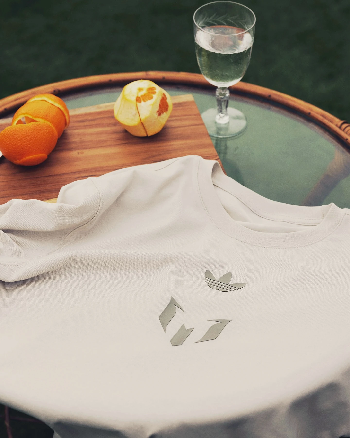 Una naranja, una copa de agua y una pieza de la nueva colaboración de Messi con adidas sobre la mesa de un living de exteriores.