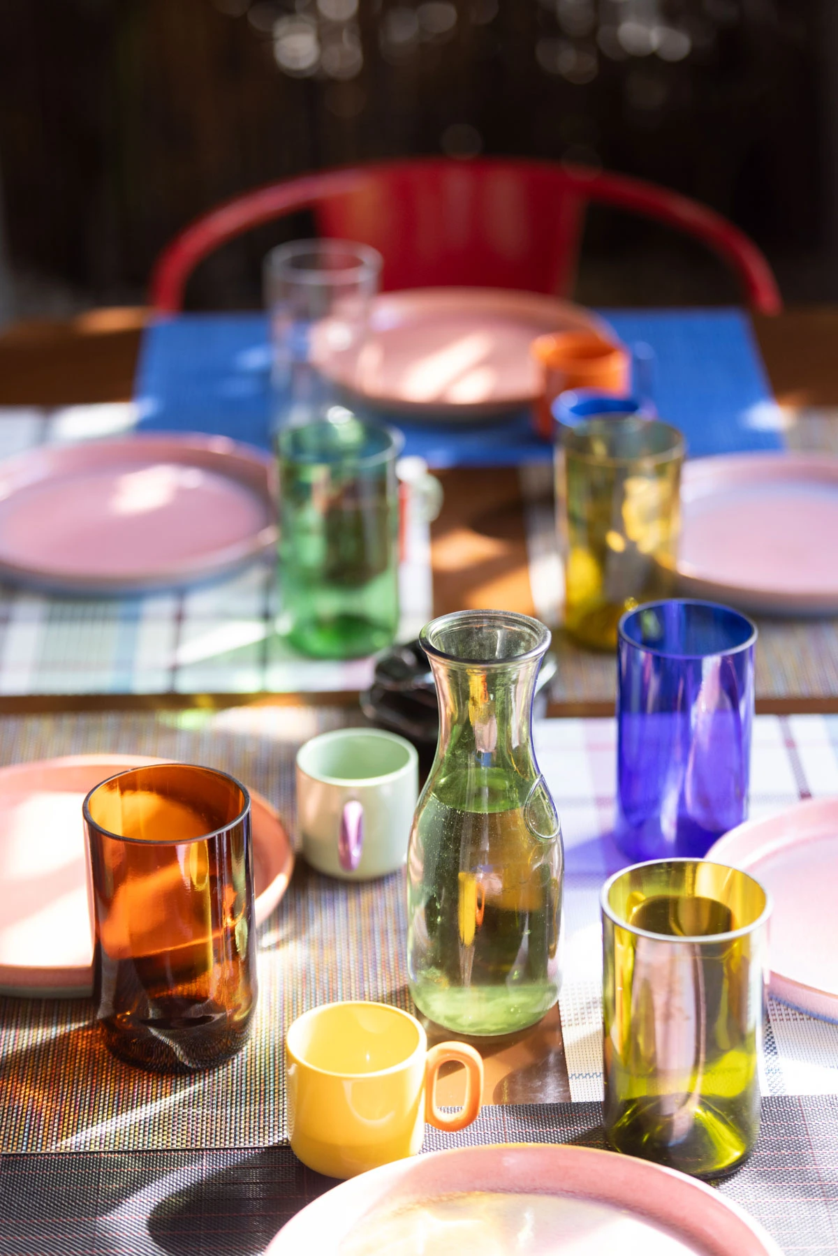 La mesa de la galeria con individuales, platos y vasos, todo de diferentes colores.