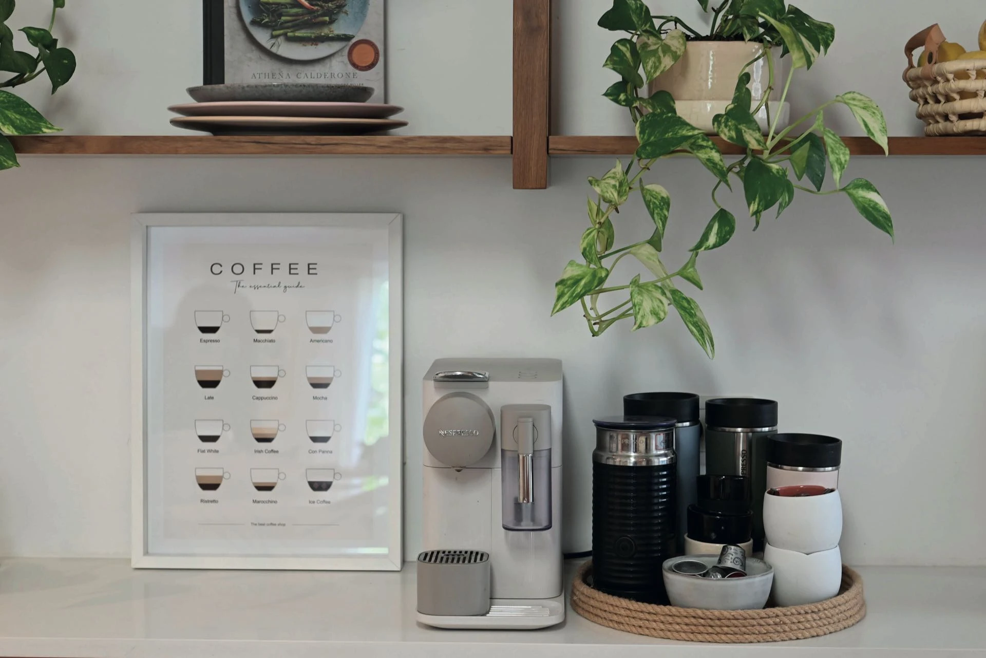 Coffee station con un cuadro, bandeja de yute con accesorios y cápsulas y una tabla de mármol y madera con tres especieros.  