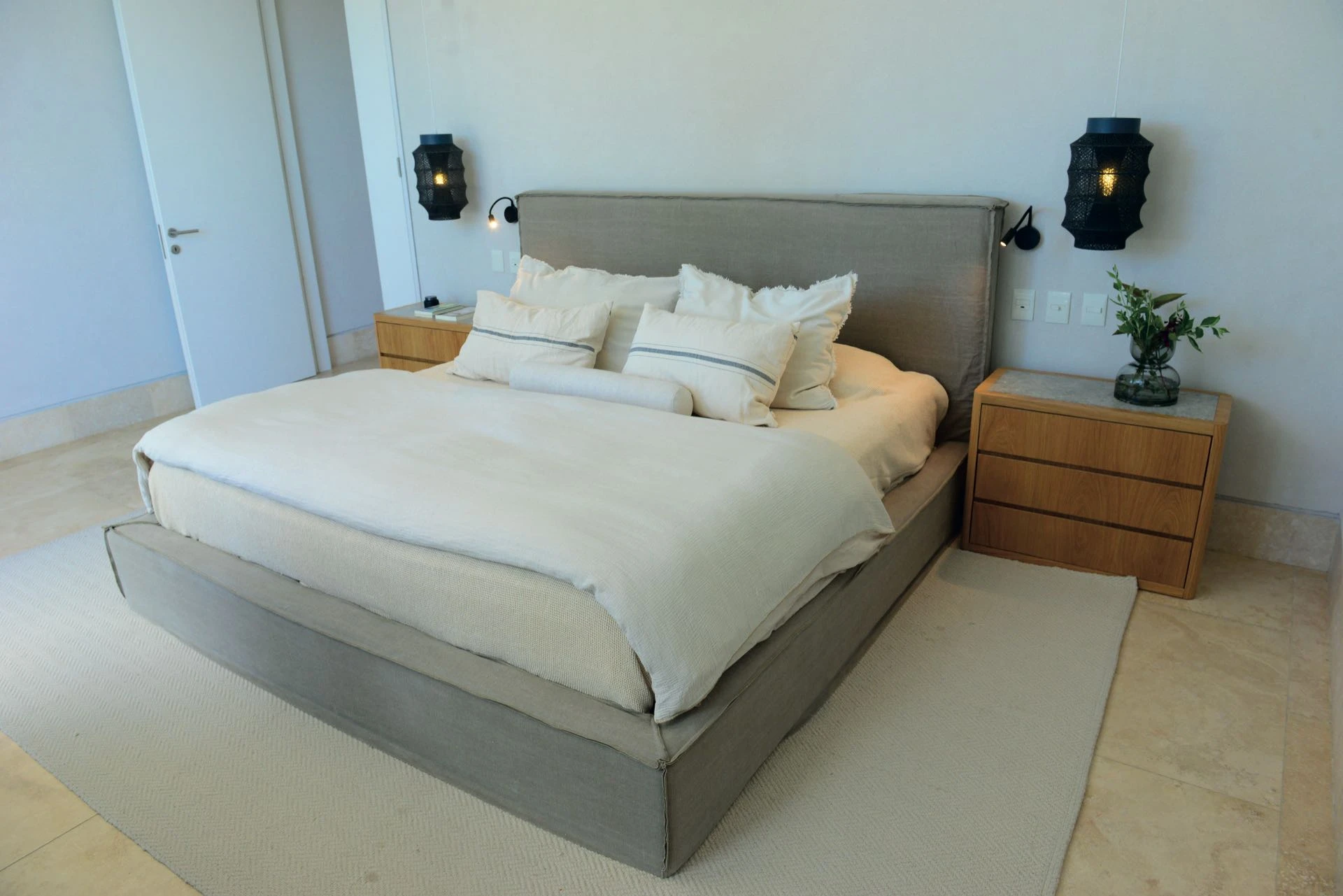 La cama estilo wabi sabi entelada en lino kotton gris piedra es protagonista.