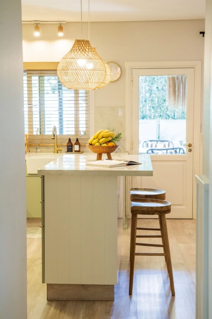 La isla revestida en madera ranurada laqueda en blanco, con taburetes de madera.  