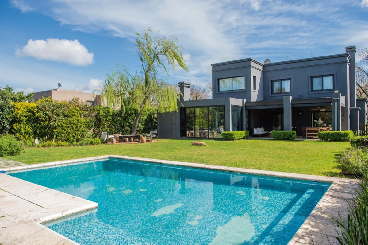 El gris oscuro de la construcción crea un marcado contraste con el verde del jardín y el azul de la pileta.