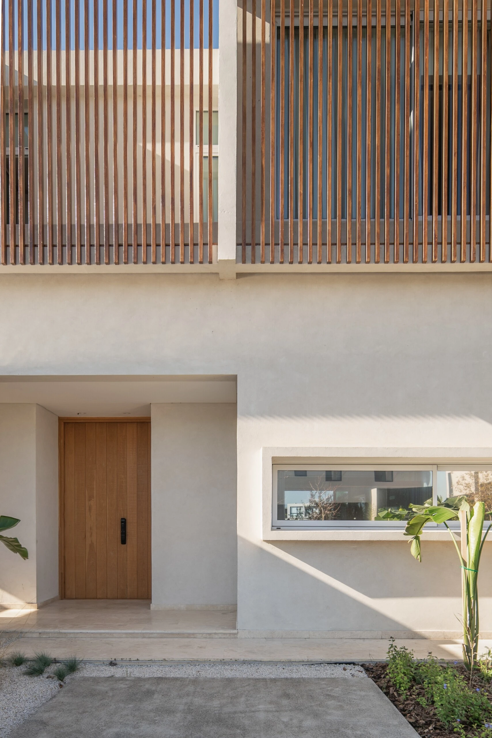 Una celosía de madera vertical actúa como un velo que filtra la luz y brinda privacidad.