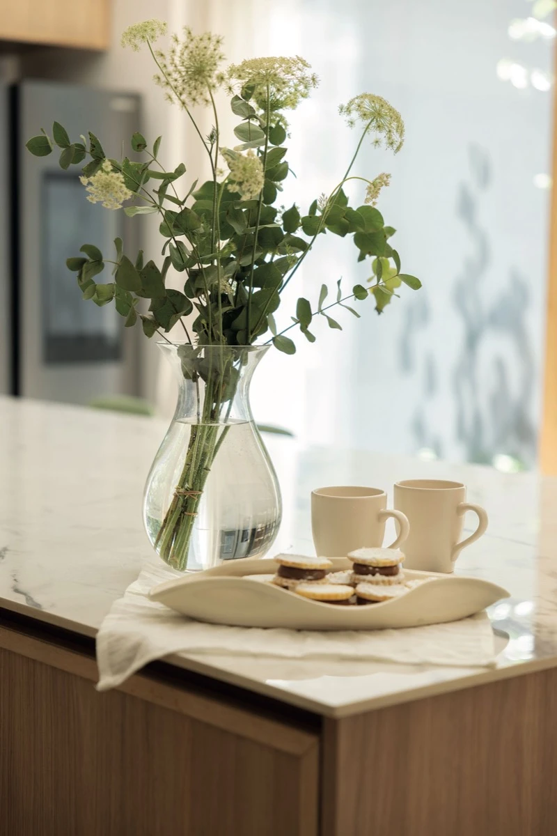 Sobre la mesada, una bandeja de cerámica irregular, tazas y un florero.  