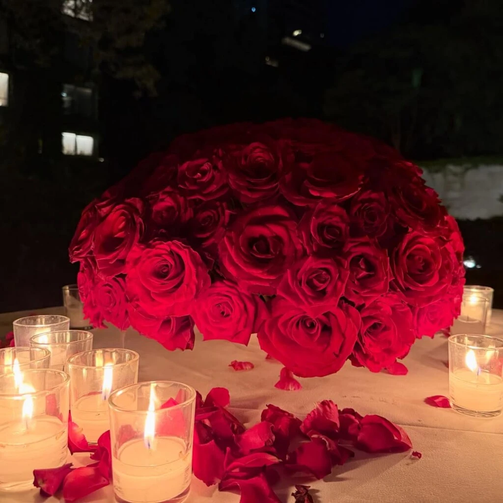 En las imágenes se puede ver una mesa redonda decorada con un gran ramo de rosas, pétalos dispersos, velas encendidas y copas de champagne.