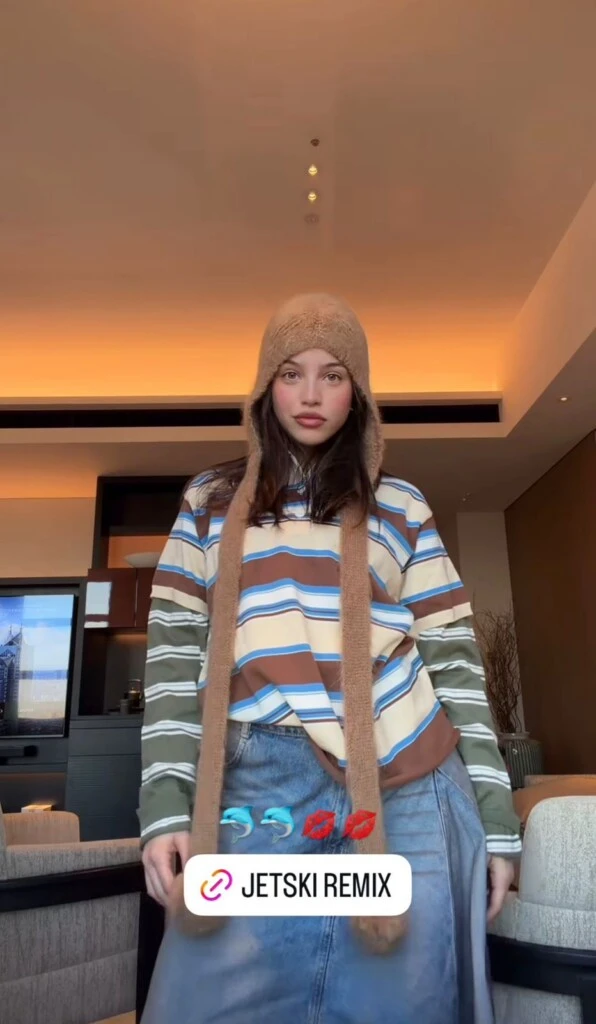 Emilia eligió un gorro tejido en tono marrón con orejeras largas tipo bufanda, una prenda muy asociada a la estética Y2K, al universo soft girl y a los looks invernales coreanos.