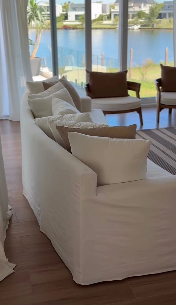 Un sillón curvo tapizado en tela clara, acompañado por almohadones en tonos tierra, suma confort y calidez. 