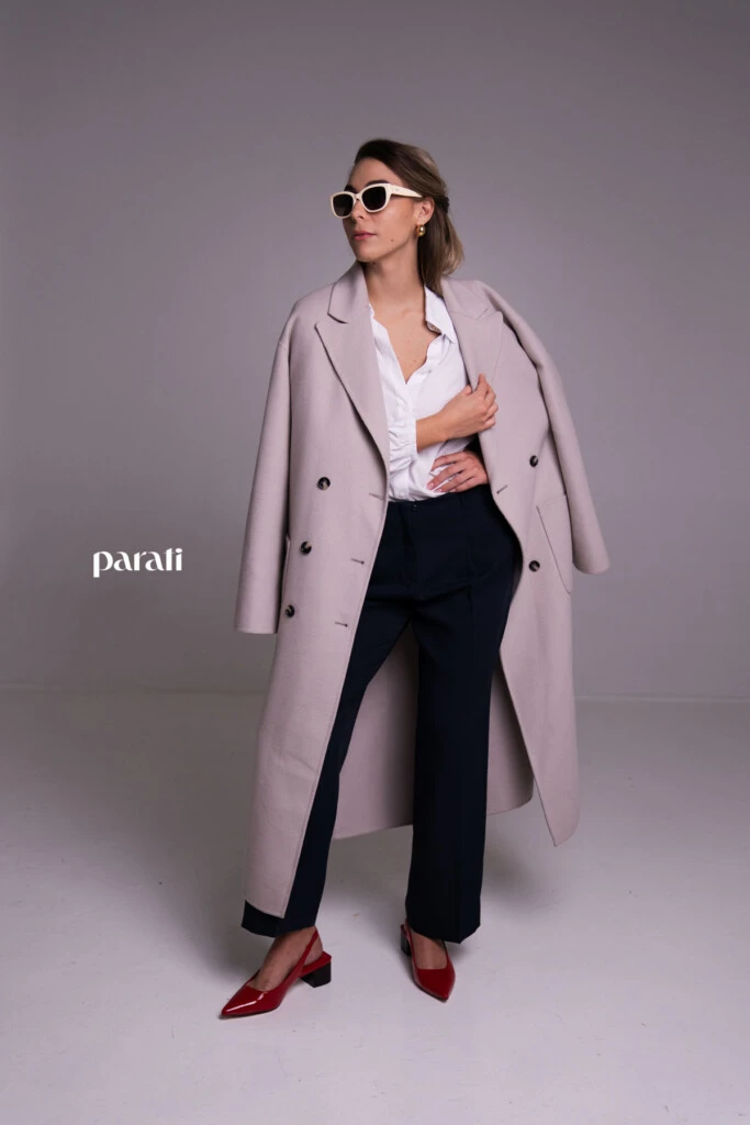 Tapado de paño cruzado color visón @mishkabuenosaires

Camisa blanca de poplín, botón con brillos @concepcion.b.a

Pantalón sastrero azul corte recto @laspepasinst

Zapatos bajos de charol rojo y sobre de cuero negro @pruneoficial

Aros dorados @tina.allo

Anteojos de marco blanco @absurda_optica