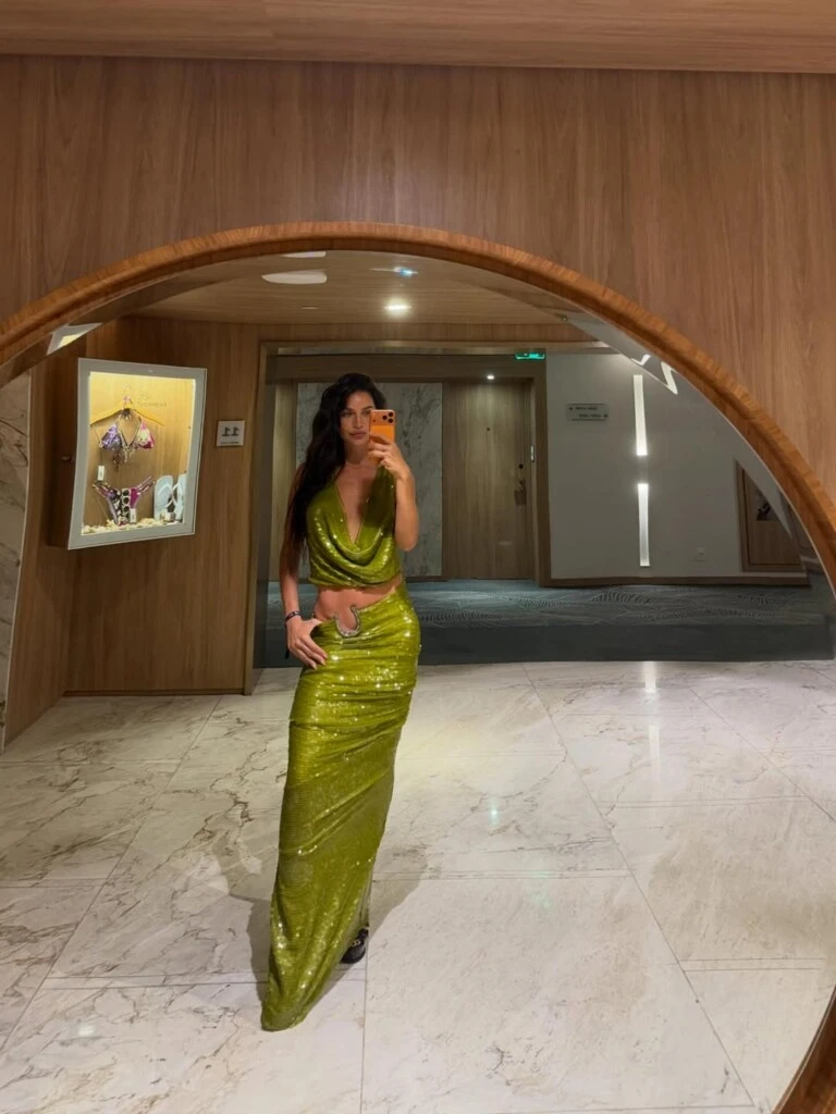 El top, con escote profundo y caída drapeada, suma sensualidad y movimiento, mientras deja al descubierto parte del abdomen, reforzando el aire relajado y canchero del outfit.