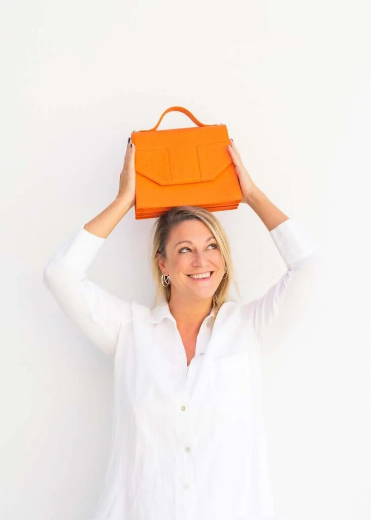 Lía Protto sostiene una cartera naranja de Tentroya en una producción que refleja el estilo creativo de la marca.