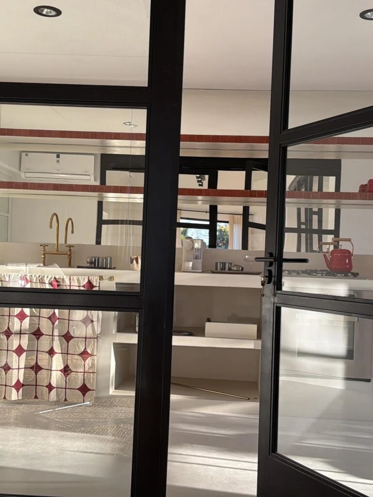La base completamente blanca se complementa con estantes de madera natural y una selección de utensilios en rojo intenso, como ollas, pavas y accesorios decorativos. 